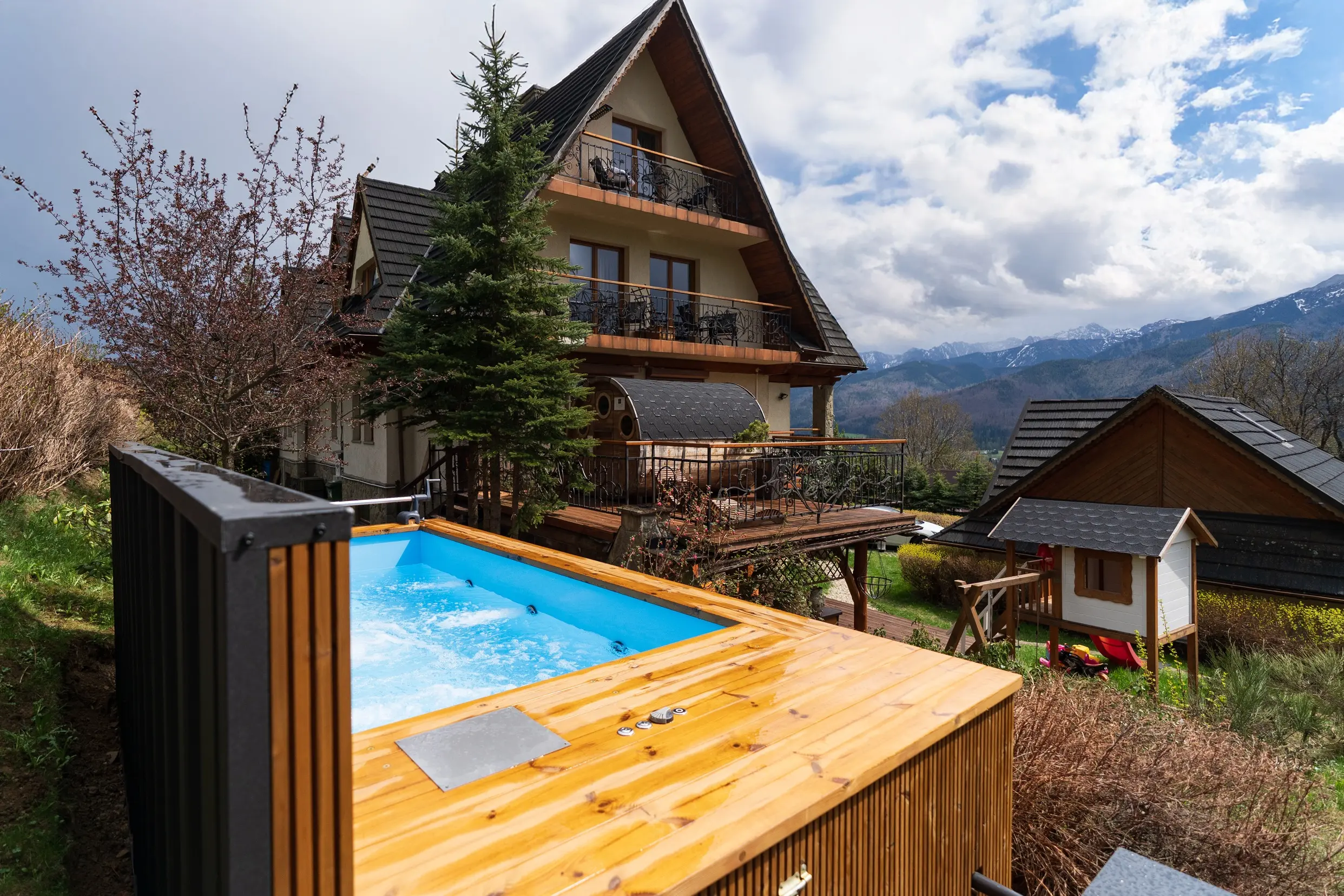Holzpool mit blauem Wasser im Garten vor Pension und Bergen